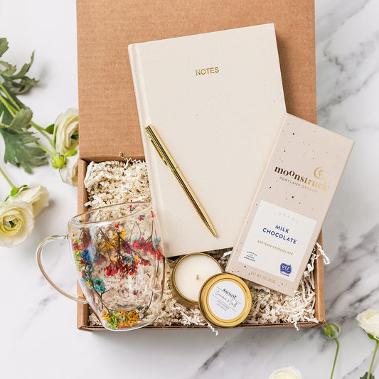 a box containing a note book, a cup of tea, a candle, and