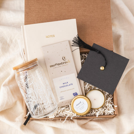 a gift box containing a candle, candle holder, and a graduation cap